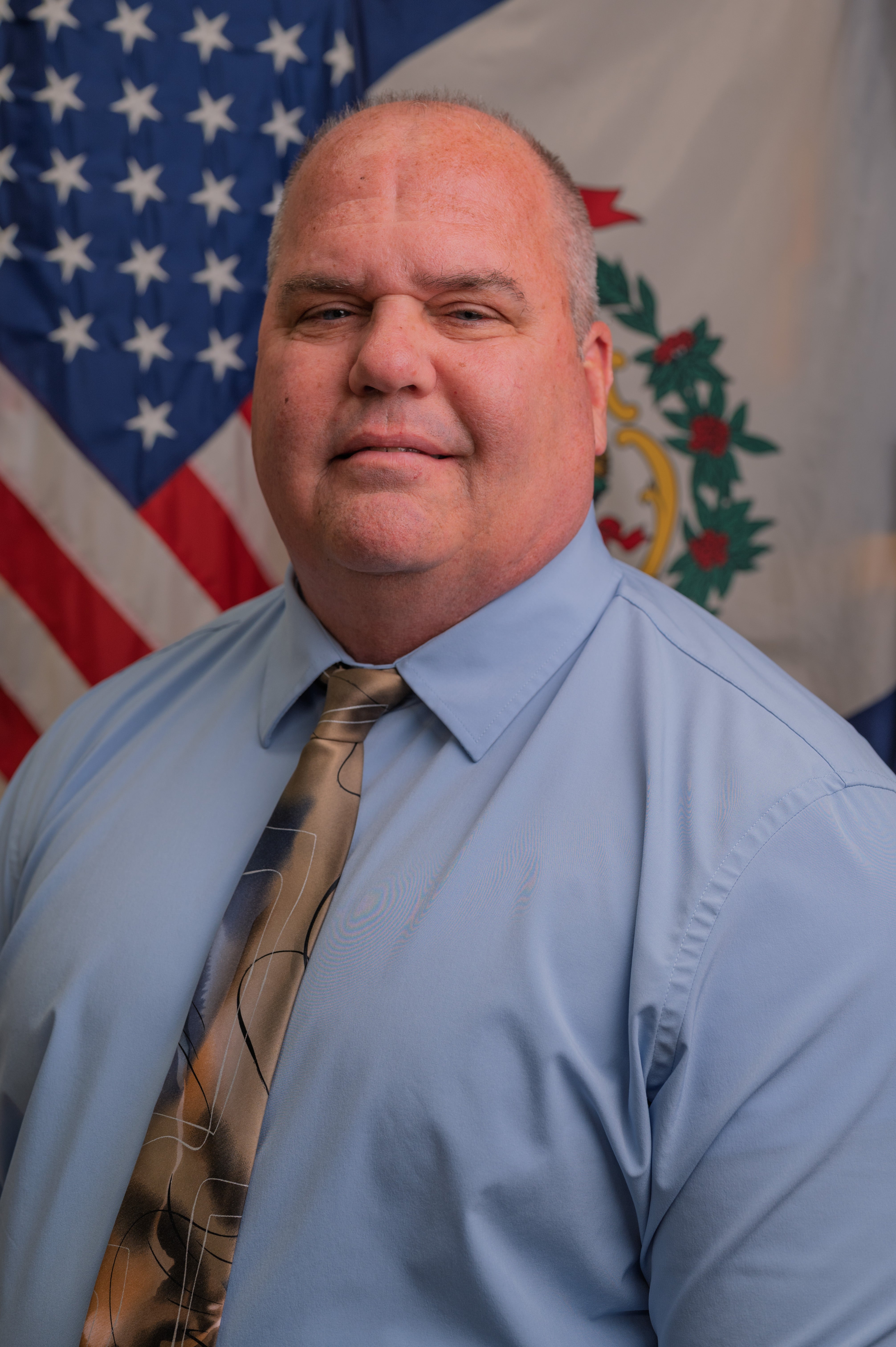 Portrait of Joseph Diedrich standing in front of American Flag and WV State Flag
