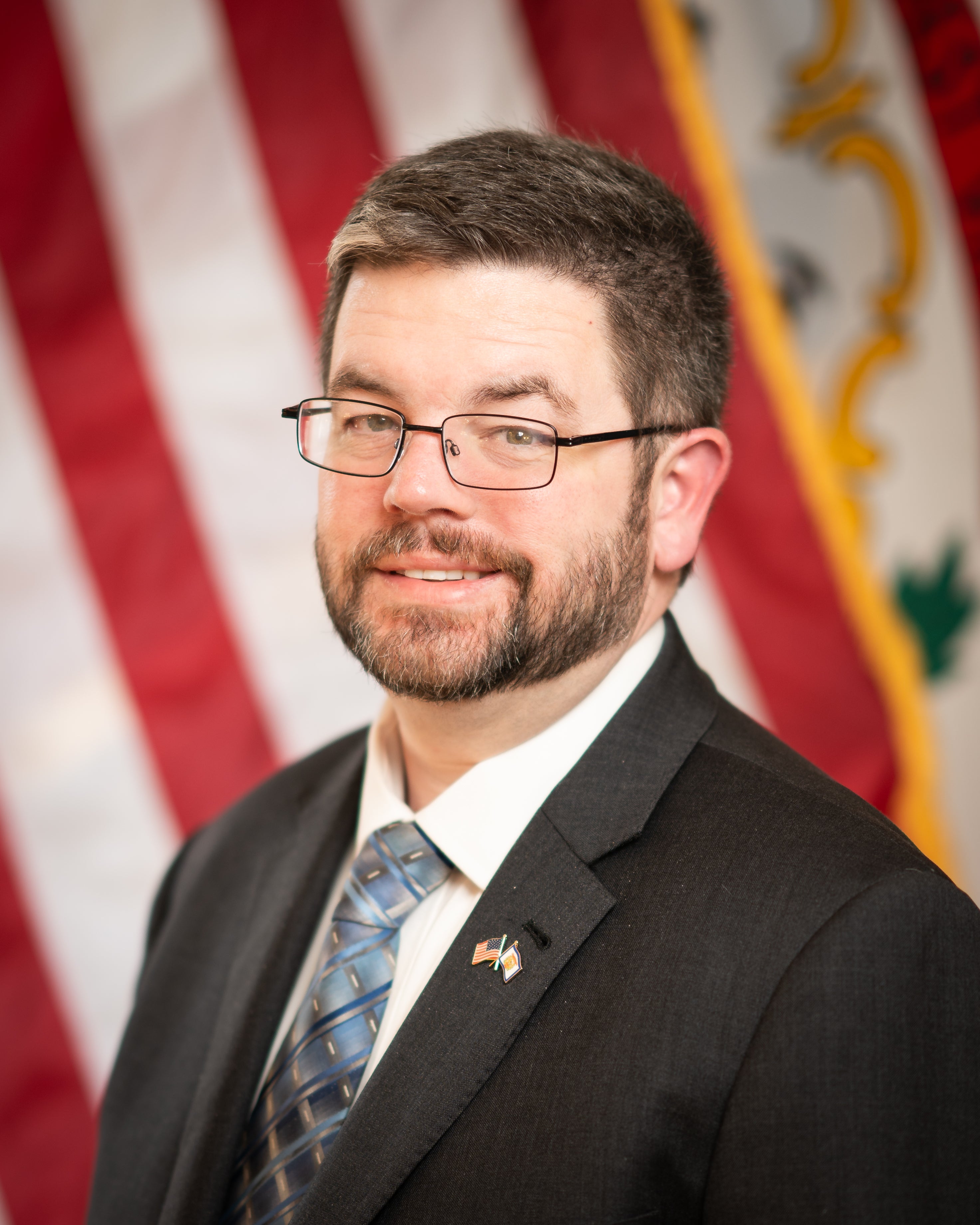 Portrait of Ryan Kennedy standing in front of American Flag and the WV State Flag