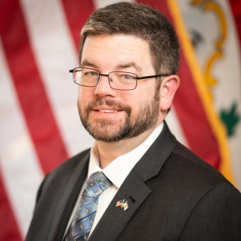Portrait of Ryan Kennedy standing in front of American Flag and the WV State Flag