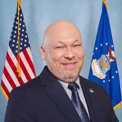 Portrait of Ron Deal standing between an American Flag and Air Force Flag